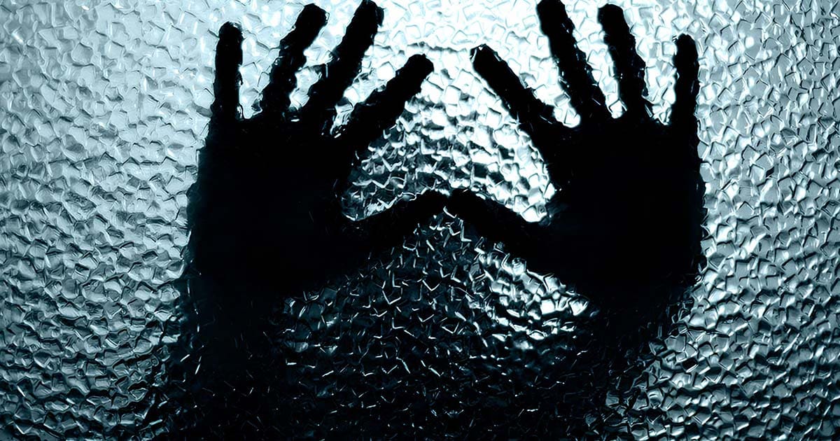 A stock image of two hands pressed against a window, illustrating the anguish experienced by hate crime survivors.