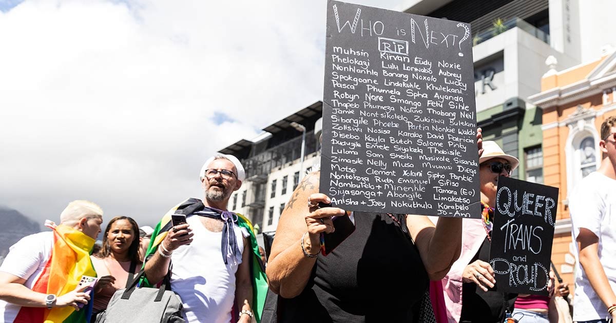 A photo of an individual holding up a placard with the many names of murdered members of the LGBT+ community.