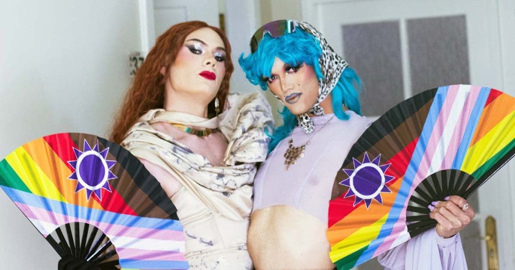 A photo of two drag performers looking fiercely at the camera while holding Namibian Pride flag fans at the launch of Celebrating Drag & Vogue Beyond Borders in Windhoek