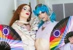 A photo of two drag performers looking fiercely at the camera while holding Namibian Pride flag fans at the launch of Celebrating Drag & Vogue Beyond Borders in Windhoek